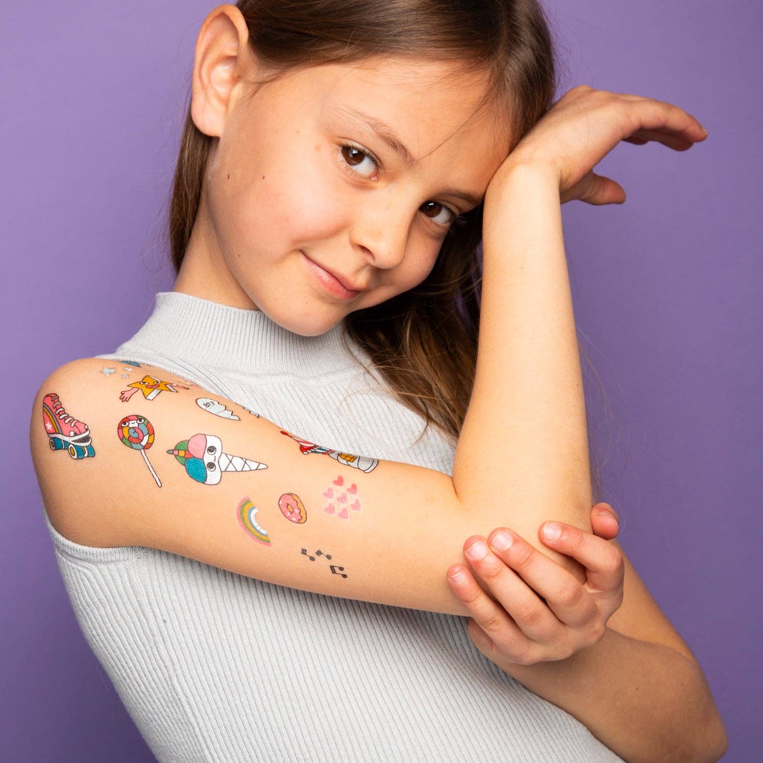 Young girl with colorful temporary tattoos on her arms against a purple background