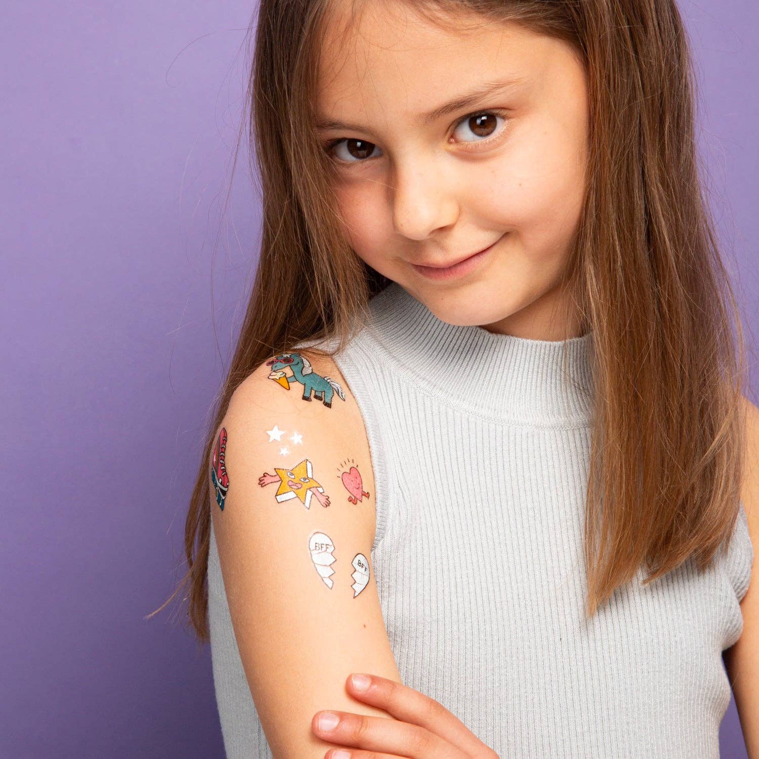 Young girl with colorful temporary tattoos on her arm against a purple background