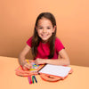 Young girl sitting at a table with a coloring book and markers, smiling against an orange background