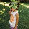 A young kid wearing pink shorts with green designs and a white tanktop with smiling cloud print.