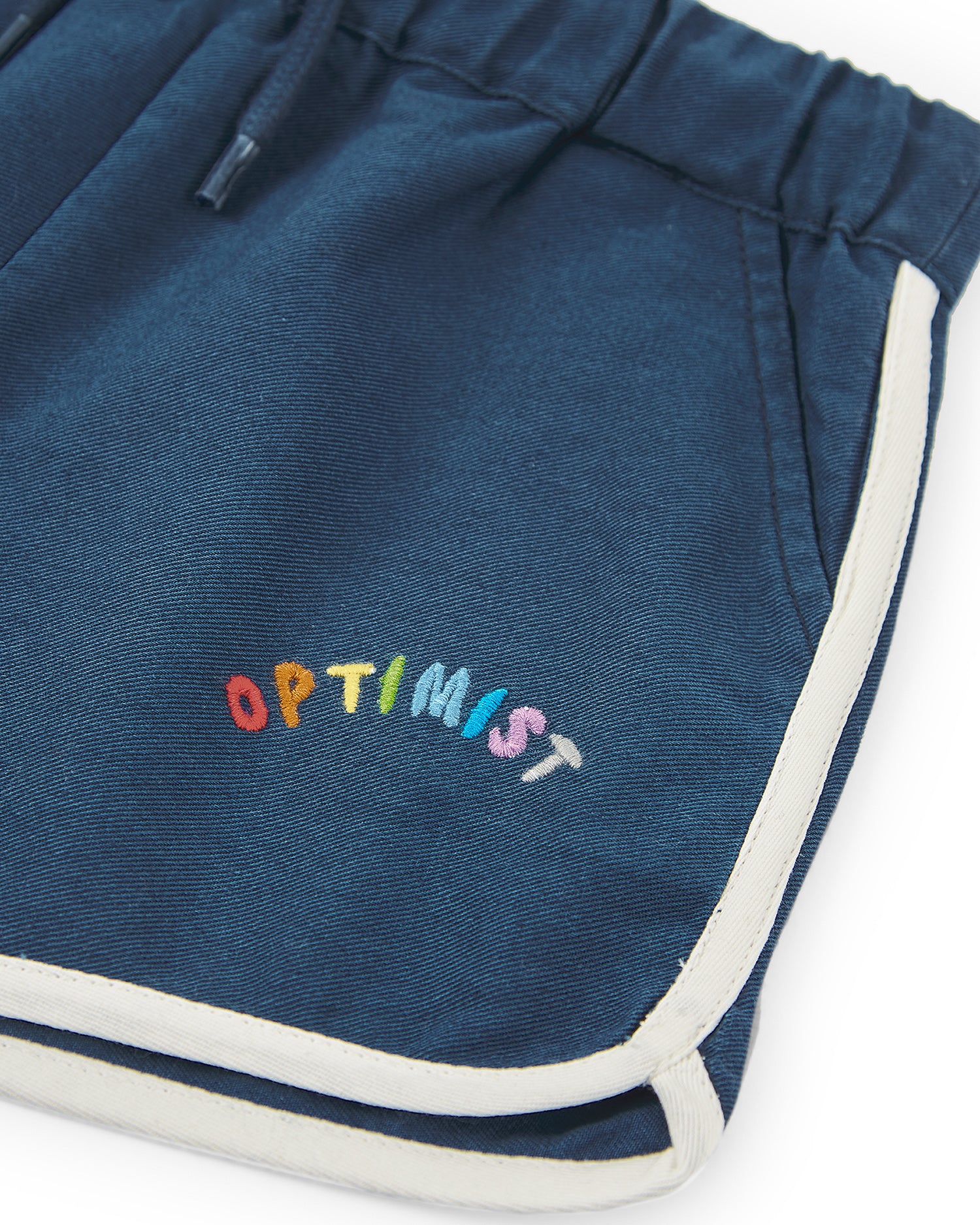 A close-up of a flat lay featuring a pair of blue track shorts with "be happy" embroidered on them